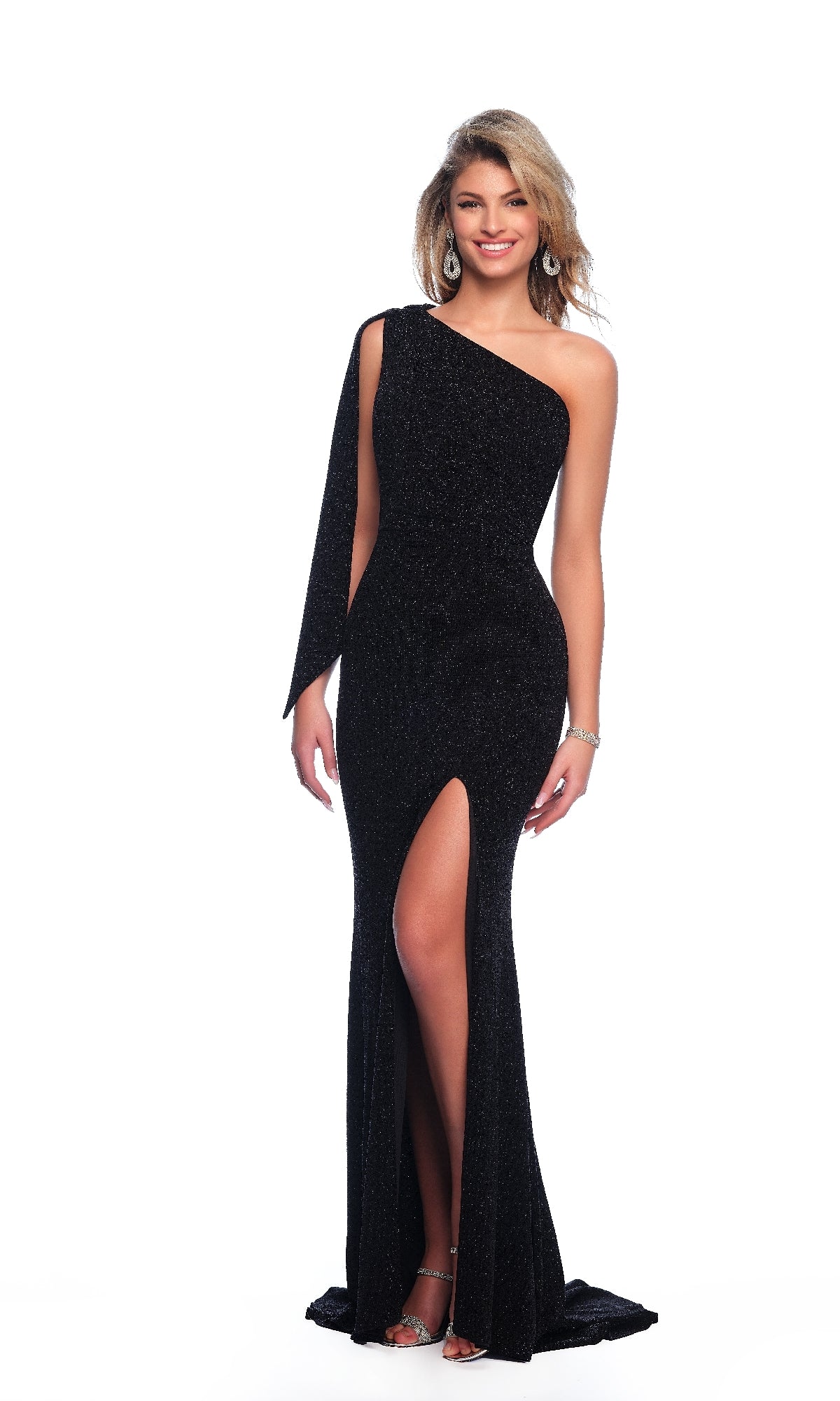 A woman poses against a white background in the Dave & Johnny 11851 one-shoulder black prom dress, featuring a thigh-high slit, paired with silver heels and statement earrings.